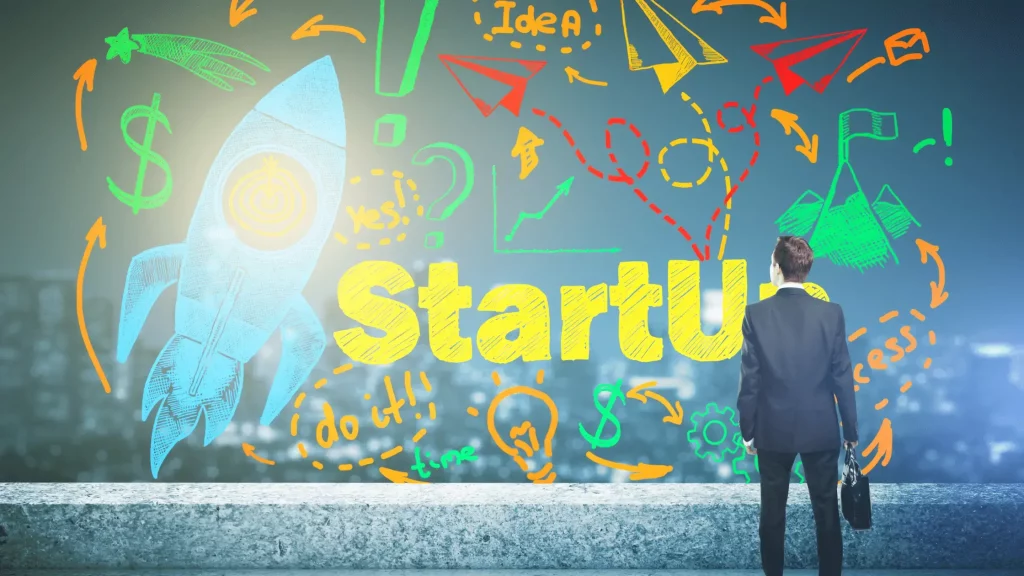 Man standing in front of rocket with 'startup' on wall. Tips to Launch A Successful Startup Business.